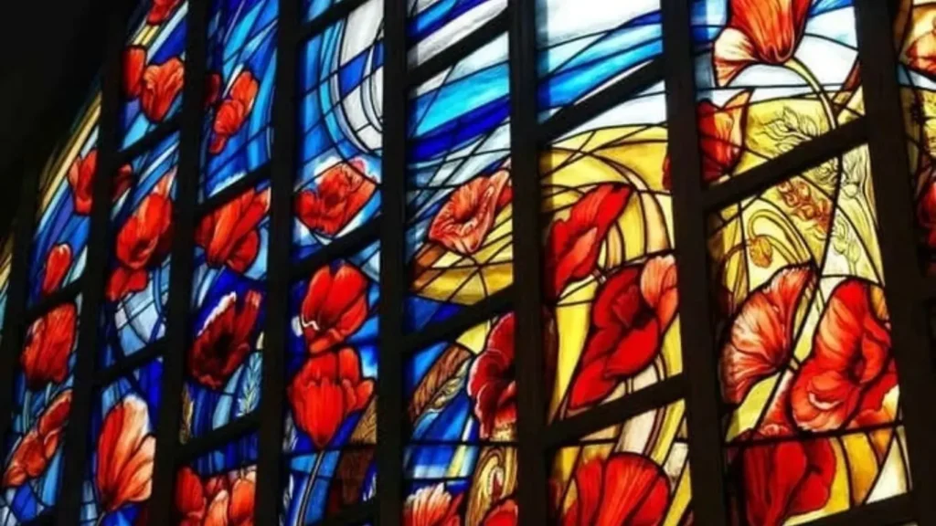 A close-up of a custom stained glass window in Dubai featuring red poppy flowers and blue swirling patterns.